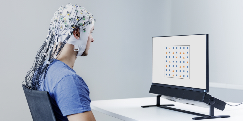 A yound man wearing EEG cap looks at a screen of Tobii Pro Spectrum eye tracker